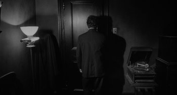 Movie still from “Eraserhead” (1977), directed by David Lynch – A black and white photo of a man standing in front of a door; Medium shot, Over the shoulder angle