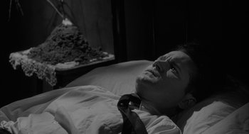 Movie still from “Eraserhead” (1977), directed by David Lynch – A man laying in a bed wearing a neck tie; Close Up shot, High angle