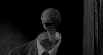 Movie still from “Eraserhead” (1977), directed by David Lynch – An image of a man in a suit and tie with a fish head in his mouth; Close Up shot, High angle