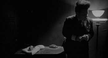 Movie still from “Eraserhead” (1977), directed by David Lynch – A black and white photo of a man standing next to a dead body; Medium shot, High angle