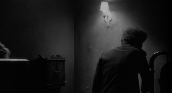 Movie still from “Eraserhead” (1977), directed by David Lynch – A man standing next to a wall in a room; Medium shot, Over the shoulder angle