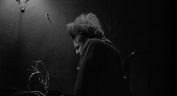Movie still from “Eraserhead” (1977), directed by David Lynch – A person with curly hair is standing in a dark room; Medium shot, Low angle