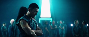 Movie still from “Escape Plan 2: Hades” (2018), directed by Steven C. Miller – A man standing in front of a group of people in a room; Medium shot, Over the shoulder angle