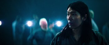 Movie still from “Escape Plan 2: Hades” (2018), directed by Steven C. Miller – A woman standing next to a crowd of people in the dark; Close Up shot, Over the shoulder angle