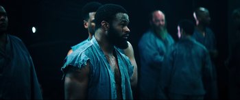 Movie still from “Escape Plan 2: Hades” (2018), directed by Steven C. Miller – A group of men standing next to each other in a dark room; Medium shot, Over the shoulder angle