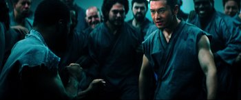 Movie still from “Escape Plan 2: Hades” (2018), directed by Steven C. Miller – A group of men standing next to each other in a room; Medium shot, Over the shoulder angle