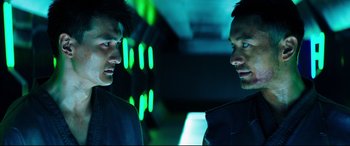 Movie still from “Escape Plan 2: Hades” (2018), directed by Steven C. Miller – A man standing next to another man in a dark room; Close Up shot, Over the shoulder angle