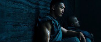 Movie still from “Escape Plan 2: Hades” (2018), directed by Steven C. Miller – A person sitting in front of a brick wall; Close Up shot, Over the shoulder angle