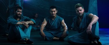 Movie still from “Escape Plan 2: Hades” (2018), directed by Steven C. Miller – A group of men sitting on the ground in a room; Medium shot, Low angle