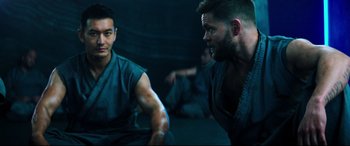 Movie still from “Escape Plan 2: Hades” (2018), directed by Steven C. Miller – Two men are sitting in a dark room and one is looking at the other; Medium shot, Over the shoulder angle