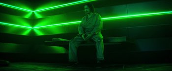 Movie still from “Escape Plan 2: Hades” (2018), directed by Steven C. Miller – A man sitting on top of a bench in a dark room; Wide shot, Low angle