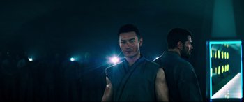 Movie still from “Escape Plan 2: Hades” (2018), directed by Steven C. Miller – A man in a blue shirt is standing in the dark; Medium shot, Low angle