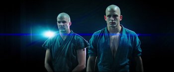 Movie still from “Escape Plan 2: Hades” (2018), directed by Steven C. Miller – Two bald men standing next to each other in front of a light; Medium shot, Low angle