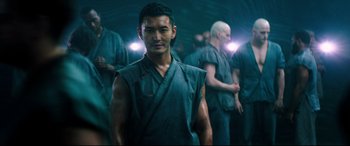 Movie still from “Escape Plan 2: Hades” (2018), directed by Steven C. Miller – A group of people in a room with lights on; Medium shot, Over the shoulder angle
