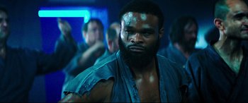 Movie still from “Escape Plan 2: Hades” (2018), directed by Steven C. Miller – A man with a beard is looking at the camera; Close Up shot, Low angle