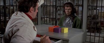 Movie still from “Escape from the Planet of the Apes” (1971), directed by Don Taylor – A man sitting at a table in front of a monkey; Medium shot, Over the shoulder angle