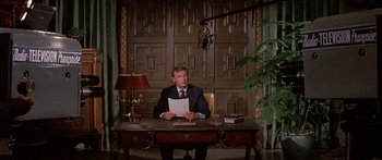 Movie still from “Escape from the Planet of the Apes” (1971), directed by Don Taylor – A man sitting at a desk in front of a microphone; Medium shot, Over the shoulder angle