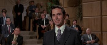 Movie still from “Escape from the Planet of the Apes” (1971), directed by Don Taylor – A man in a suit and tie in front of a group of people; Close Up shot, Over the shoulder angle