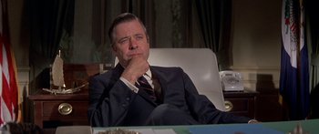 Movie still from “Escape from the Planet of the Apes” (1971), directed by Don Taylor – A man in a suit and tie sitting in a chair with his hand on his chin; Close Up shot, Low angle