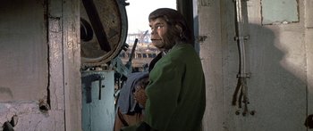 Movie still from “Escape from the Planet of the Apes” (1971), directed by Don Taylor – A man dressed as a monkey standing next to a building; Medium shot, Over the shoulder angle