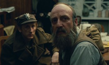 Movie still from “Europa Europa” (1990), directed by Agnieszka Holland – A man with a beard sitting next to another man with a hat; Close Up shot, Over the shoulder angle