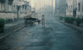 Movie still from “Europa Europa” (1990), directed by Agnieszka Holland – A woman standing in a street with a cart in the background; Wide shot, High angle