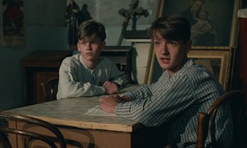 Movie still from “Europa Europa” (1990), directed by Agnieszka Holland – Two young men sitting at a table in front of a crucifix; Medium shot, Over the shoulder angle