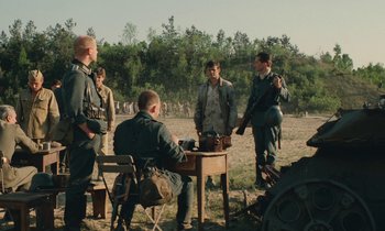 Movie still from “Europa Europa” (1990), directed by Agnieszka Holland – A group of men standing next to each other on top of a dirt field; Wide shot, Over the shoulder angle