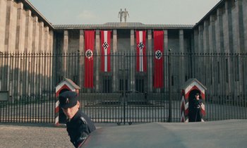 Movie still from “Europa Europa” (1990), directed by Agnieszka Holland – A man in a police uniform standing in front of a building; Extreme Wide shot, Low angle