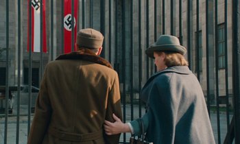 Movie still from “Europa Europa” (1990), directed by Agnieszka Holland – A couple of people that are walking by a gate; Medium shot, Over the shoulder angle