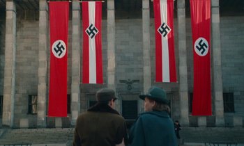 Movie still from “Europa Europa” (1990), directed by Agnieszka Holland – Two people are standing in front of a building with nazi flags; Extreme Wide shot, Low angle