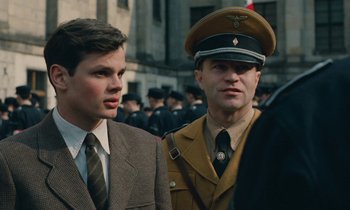 Movie still from “Europa Europa” (1990), directed by Agnieszka Holland – Two young men in suits and military garb stand next to each other in front of a crowd; Close Up shot, Over the shoulder angle