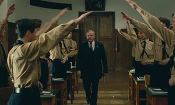 Movie still from “Europa Europa” (1990), directed by Agnieszka Holland – A man in a black suit walking in front of a group of people; Wide shot, Low angle