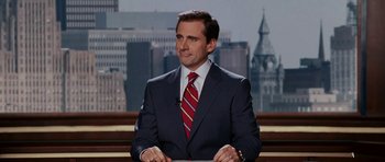 Movie still from “Evan Almighty” (2007), directed by Tom Shadyac – A man wearing a suit and tie sitting in front of a building; Medium shot, Low angle