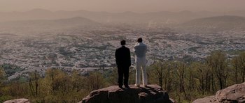 Two men standing on top of a hill looking at a city