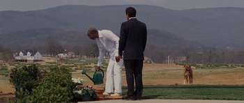 Movie still from “Evan Almighty” (2007), directed by Tom Shadyac – A man in a white suit and a man in a black suit stand next to a watering can; Wide shot, Over the shoulder angle