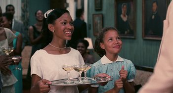 Movie still from “Eve's Bayou” (1997), directed by Kasi Lemmons – Two young women holding a tray with champagne glasses on top of it; Medium shot, Over the shoulder angle