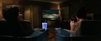 Movie still from “El Camino: A Breaking Bad Movie” (2019), directed by Vince Gilligan – Two people sitting in front of a television; Wide shot, High angle