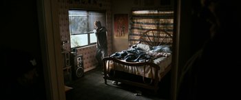 Movie still from “El Camino: A Breaking Bad Movie” (2019), directed by Vince Gilligan – A man standing next to a bed looking out a window; Wide shot, High angle