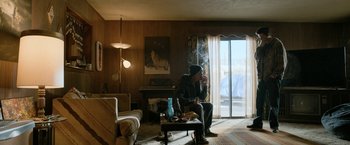 Movie still from “El Camino: A Breaking Bad Movie” (2019), directed by Vince Gilligan – A man sitting in a living room smoking a cigarette; Wide shot, Over the shoulder angle