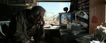 Movie still from “El Camino: A Breaking Bad Movie” (2019), directed by Vince Gilligan – An older man on the phone in front of a tv; Medium shot, Low angle
