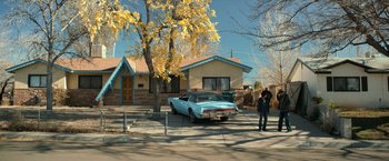 Movie still from “El Camino: A Breaking Bad Movie” (2019), directed by Vince Gilligan – A man standing in front of a car parked in front of a house; Extreme Wide shot, Low angle