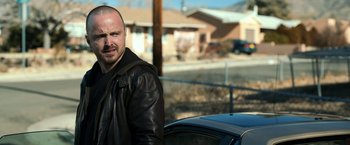 Movie still from “El Camino: A Breaking Bad Movie” (2019), directed by Vince Gilligan – A man standing next to a car in a parking lot; Close Up shot, Over the shoulder angle