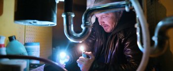 Movie still from “El Camino: A Breaking Bad Movie” (2019), directed by Vince Gilligan – A man in leather jacket looking at a cell phone in front of a sink; Close Up shot, Low angle