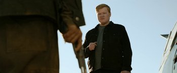 Movie still from “El Camino: A Breaking Bad Movie” (2019), directed by Vince Gilligan – A man standing next to another man holding a gun; Medium shot, Over the shoulder angle