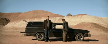 Movie still from “El Camino: A Breaking Bad Movie” (2019), directed by Vince Gilligan – Two men standing in front of an old black car; Wide shot, Low angle