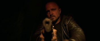 Movie still from “El Camino: A Breaking Bad Movie” (2019), directed by Vince Gilligan – A man is holding a gun in a dark room; Close Up shot, Low angle