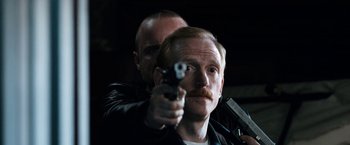 Movie still from “El Camino: A Breaking Bad Movie” (2019), directed by Vince Gilligan – A man holding a gun in front of another man; Close Up shot, Low angle