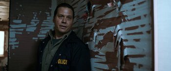 Movie still from “El Camino: A Breaking Bad Movie” (2019), directed by Vince Gilligan – A man in a police uniform standing in front of a wall; Close Up shot, Low angle