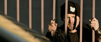 Movie still from “El Camino: A Breaking Bad Movie” (2019), directed by Vince Gilligan – A man holding a cell phone behind a fence; Close Up shot, Low angle